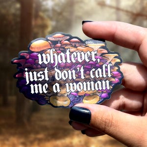 Puede incluir: Una pegatina con un diseño de setas en tonos naranja, morado y marrón. El texto de la pegatina dice: "whatever, just don't call me a woman".