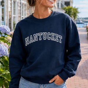 Puede incluir: Una sudadera azul marino de manga larga con cuello redondo que presenta la palabra NANTUCKET impresa en letras may&uacute;sculas blancas con una fuente arqueada en el pecho. La prenda es de tela de color s&oacute;lido y tiene cuello, pu&ntilde;os y dobladillo acanalados.