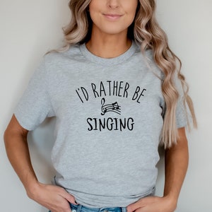 以下が含まれることがあります： 「I'd rather be singing」というテキストと音符のグラフィックがプリントされたグレーのTシャツです。