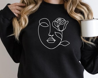 May include: Black sweatshirt with a white line drawing of a face with a rose in its eye.