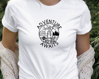 Könnte beinhalten: Weißes T-Shirt mit einer schwarz-weißen Grafik eines Wohnmobils, Bergen und einer Sonne. Die Grafik befindet sich in einem Kreis mit dem Text "Adventure Awaits" darum herum.