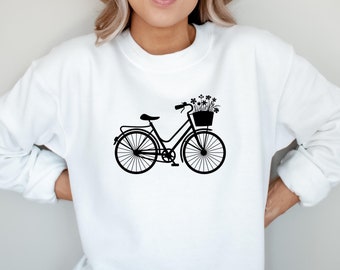 Puede incluir: Sudadera blanca con una silueta negra de una bicicleta con una cesta de flores en la parte delantera.