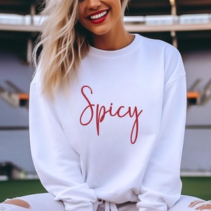 May include: White sweatshirt with the word "Spicy" written in red cursive lettering.
