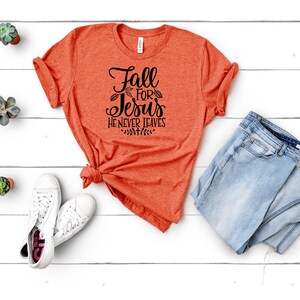K&ouml;nnte beinhalten: Orangefarbenes T-Shirt mit dem Text "Fall for Jesus He Never Leaves" in schwarzer Schrift.