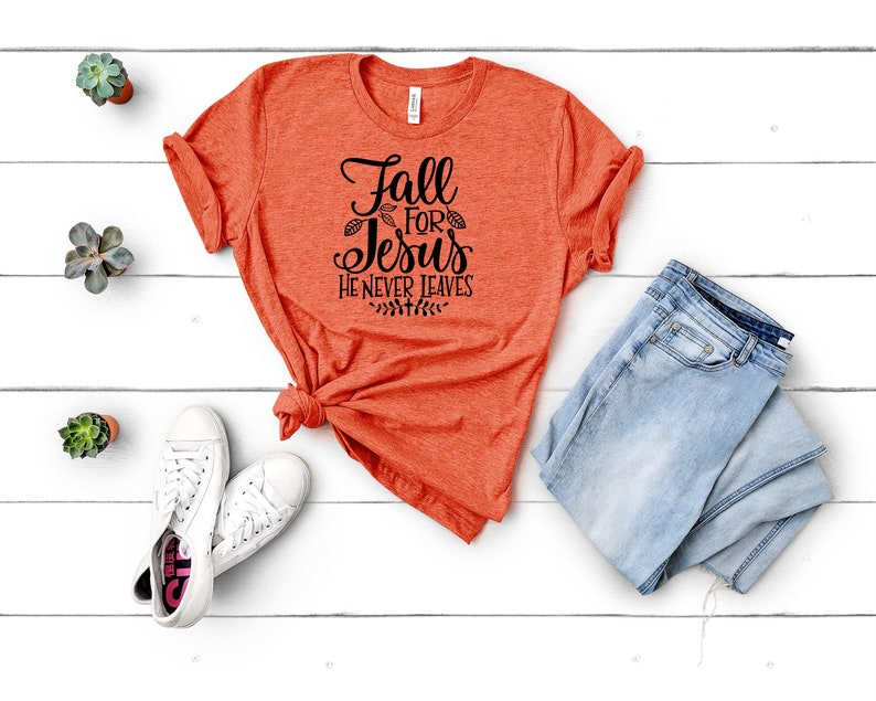 K&ouml;nnte beinhalten: Orangefarbenes T-Shirt mit dem Text "Fall for Jesus He Never Leaves" in schwarzer Schrift.