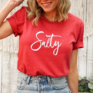 May include: Red t-shirt with the word "Salty" written in white cursive lettering.