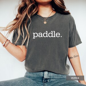 A person wearing a pepper gray t-shirt with the word paddle printed in white on the chest.