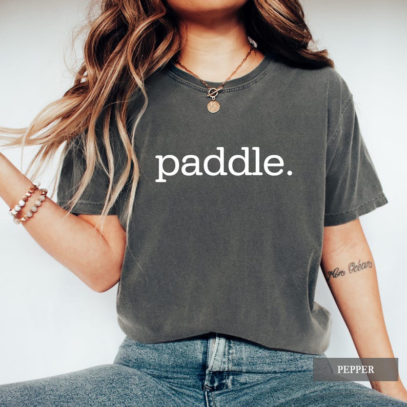 A person wearing a pepper gray t-shirt with the word paddle printed in white on the chest.