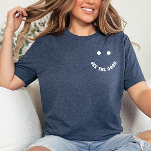 K&ouml;nnte beinhalten: Ein marineblaues T-Shirt mit einem wei&szlig;en Smiley und dem Text "See the good" auf der Vorderseite.