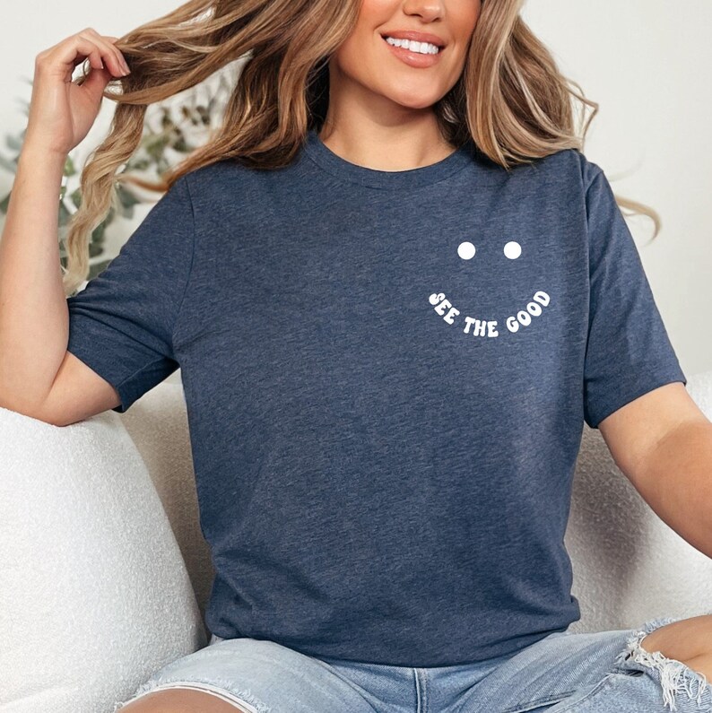 K&ouml;nnte beinhalten: Ein marineblaues T-Shirt mit einem wei&szlig;en Smiley und dem Text "See the good" auf der Vorderseite.