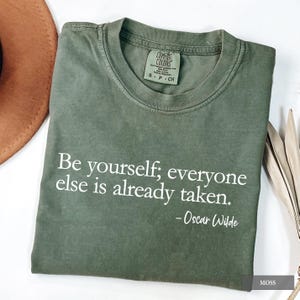 An olive green Comfort Colors t-shirt printed with the quote "Be yourself; everyone else is already taken. - Oscar Wilde" in white lettering.