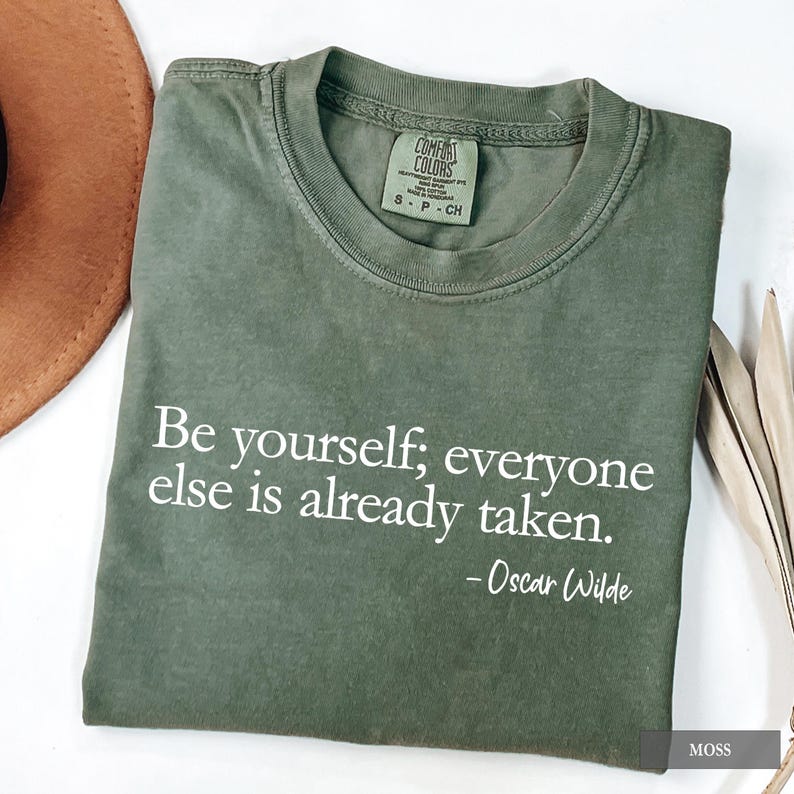 An olive green Comfort Colors t-shirt printed with the quote "Be yourself; everyone else is already taken. - Oscar Wilde" in white lettering.