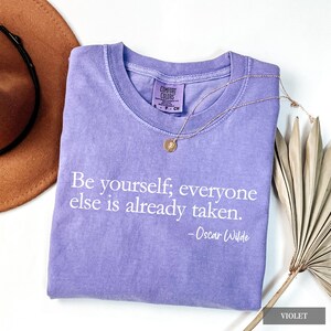 A violet Comfort Colors t-shirt printed with the quote "Be yourself; everyone else is already taken. - Oscar Wilde" in white lettering.