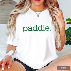 A person wearing a white t-shirt with the word paddle printed in green on the chest.
