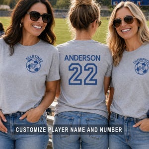 May include: Three women wearing gray t-shirts with soccer-themed designs. Each shirt features a name and number, with a soccer ball graphic. The text "CUSTOMIZE PLAYER NAME AND NUMBER" is displayed at the bottom.