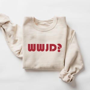 May include: A beige sweatshirt with the text "WWJD?" printed in red on the front.