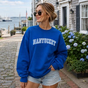 Puede incluir: Una sudadera de cuello redondo en color azul real con la palabra NANTUCKET impresa en letras may&uacute;sculas blancas en el pecho con una tipograf&iacute;a de estilo universitario. La prenda tiene mangas largas, cuello acanalado y un corte holgado.