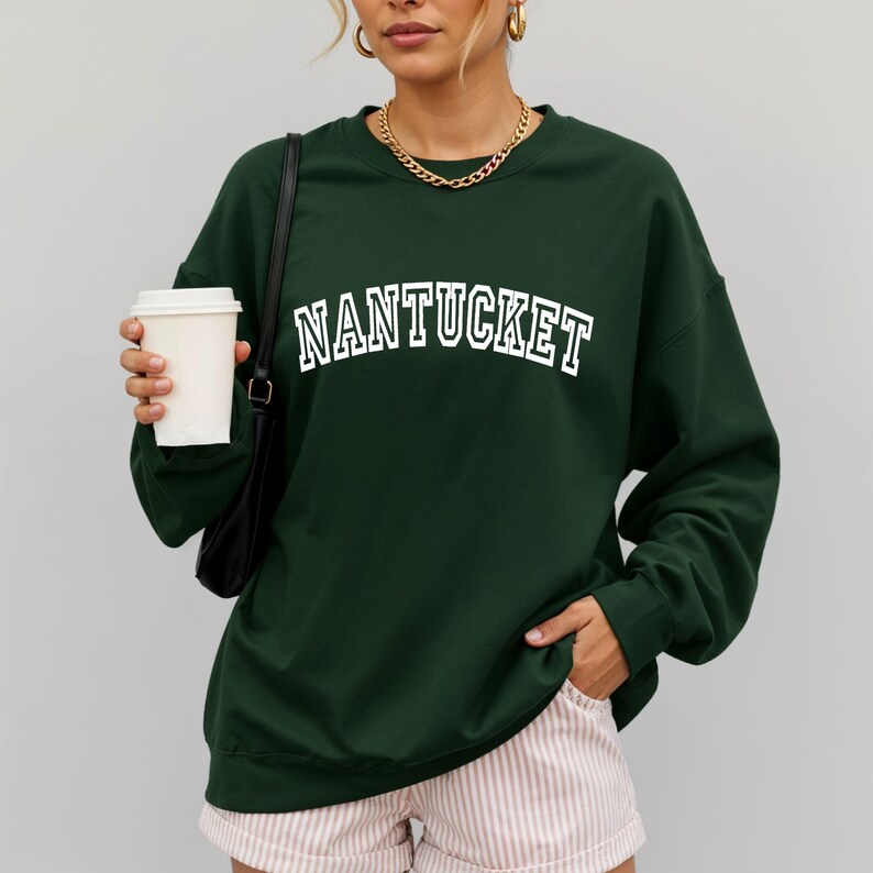 Puede incluir: Una sudadera de manga larga y cuello redondo en color verde oscuro con la palabra NANTUCKET impresa en letras blancas de bloque en el pecho. La prenda tiene un corte holgado con pu&ntilde;os y cuello acanalados, combinada con pantalones cortos de rayas claros.