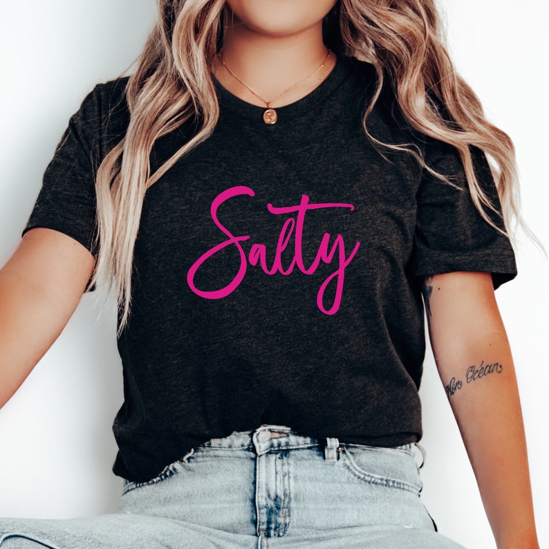 May include: A dark gray t-shirt with the word "Salty" written in pink cursive lettering.