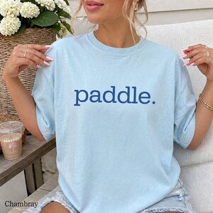 A person wearing a light blue t-shirt with the word paddle printed in dark blue on the chest.