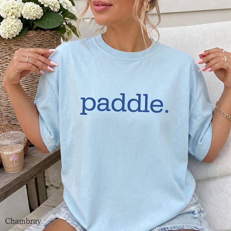 A person wearing a light blue t-shirt with the word paddle printed in dark blue on the chest.
