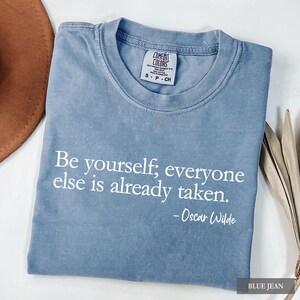 A blue-grey Comfort Colors t-shirt printed with the quote "Be yourself; everyone else is already taken. - Oscar Wilde" in white lettering.
