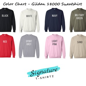 May include: Color chart showing different colors of Gildan 18000 sweatshirts. The colors include black, white, navy, military green, red, sport grey, light pink, and sand.