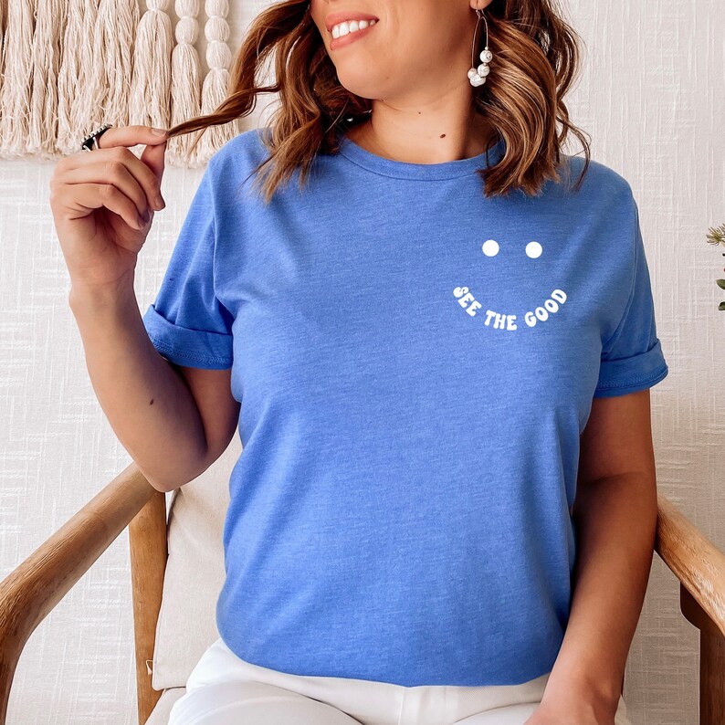 K&ouml;nnte beinhalten: Ein blaues T-Shirt mit einem wei&szlig;en Smiley und dem Text "SEE THE GOOD" auf der Vorderseite.