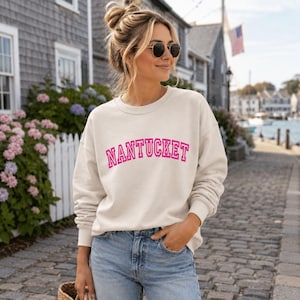 Puede incluir: Una sudadera de cuello redondo color crema con la palabra NANTUCKET impresa en el pecho en una fuente de estilo universitario de color rosa intenso, arqueada y llamativa. La prenda tiene mangas largas con pu&ntilde;os acanalados y un cuello acanalado.