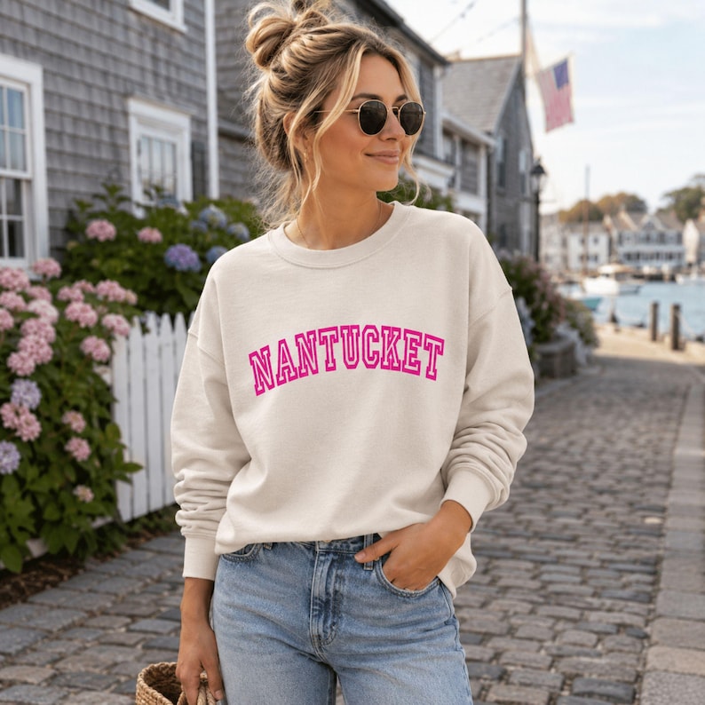Puede incluir: Una sudadera de cuello redondo color crema con la palabra NANTUCKET impresa en el pecho en una fuente de estilo universitario de color rosa intenso, arqueada y llamativa. La prenda tiene mangas largas con pu&ntilde;os acanalados y un cuello acanalado.