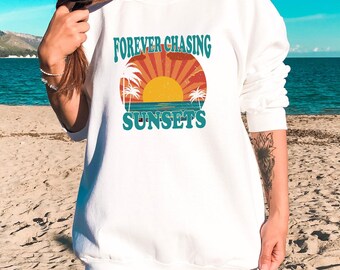 May include: White sweatshirt with a graphic print of a sunset with palm trees and the text "FOREVER CHASING SUNSETS".