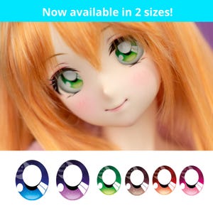 May include: A doll with orange hair and green eyes. The image includes a selection of doll eye designs in various colors, including blue, purple, green, brown, orange, and pink. Text at the top reads "Now available in 2 sizes!"
