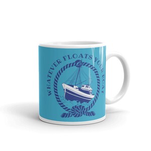Könnte beinhalten: Eine weiße Keramiktasse mit blauem Hintergrund und einer marineblauen Grafik eines Bootes in einem Seilkranz. Der Text "Whatever Floats Your Boat" ist um den Kranz herum geschrieben.