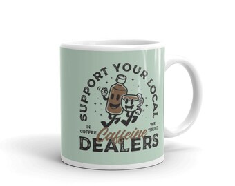 May include: A white ceramic mug with a green background and a cartoon illustration of a coffee bottle and a coffee cup running. The text reads "Support Your Local In Coffee We Trust Caffeine Dealers".