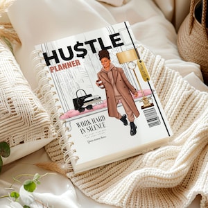 May include: A white planner with a black and gold title "Hustle Planner". The cover features a cartoon illustration of a woman in a brown coat and black pants holding a coffee cup. The text "Work hard in silence" is printed below the illustration.