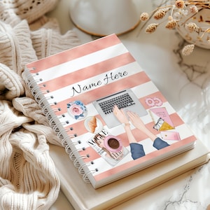 May include: A pink and white striped spiral bound notebook with the text "Name Here" on the cover. The notebook features a laptop, coffee cup, magazine, and other accessories.