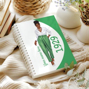 May include: A spiral-bound notebook with a green and white cover featuring an illustration of a person in green pants and a white shirt. The cover also includes the year "1929" and the text "Your name here."