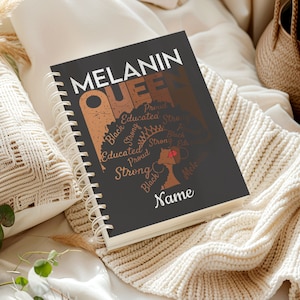 May include: A spiral-bound notebook with a black cover featuring the words "MELANIN QUEEN" in white and brown. The design includes a silhouette of a woman with a crown and the words "Proud," "Educated," and "Strong."