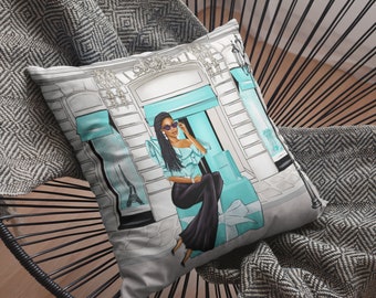 May include: A decorative throw pillow with a white background featuring a woman wearing sunglasses and a blue dress standing in front of a turquoise storefront with a large gift box. The storefront has a sign that says "Tiffany & Co."