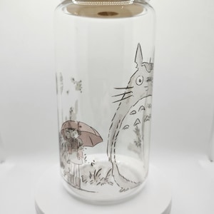 May include: A clear glass jar with a bamboo lid features a black and white illustration of a character from the animated film "My Neighbor Totoro". The character is standing next to a girl holding an umbrella.