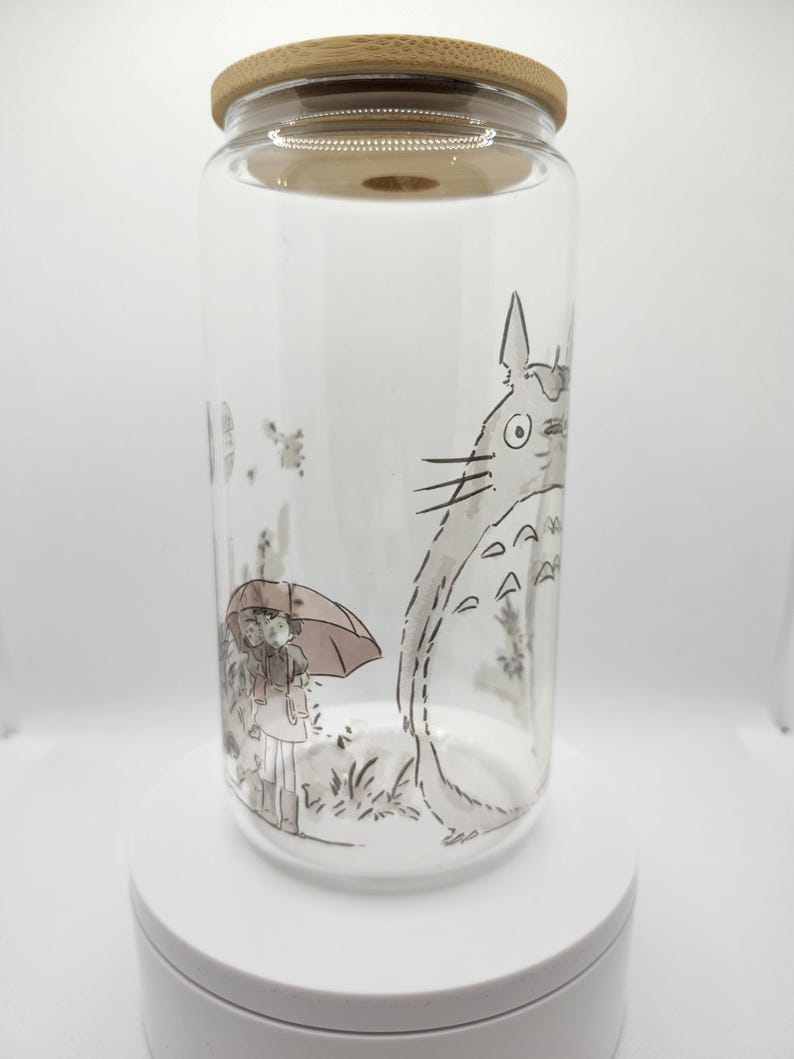 May include: A clear glass jar with a bamboo lid features a black and white illustration of a character from the animated film "My Neighbor Totoro". The character is standing next to a girl holding an umbrella.