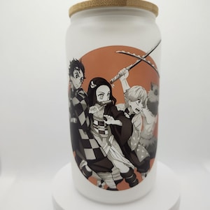 Peut inclure: Boîte en céramique blanche avec un couvercle en bambou représentant un graphique de trois personnages d'anime avec des épées dans un cercle rouge et orange. Les personnages sont en noir et blanc.
