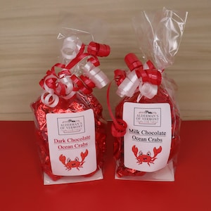 May include: Two bags of chocolate ocean crabs, one bag is dark chocolate and the other is milk chocolate. Both bags are tied with red and white ribbon and have a label with the company name "Alderman's of Vermont" and a cartoon crab.