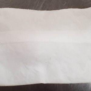 May include: A white, rectangular, fabric pouch with a seam down the center.