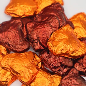 May include: A pile of heart-shaped chocolates wrapped in foil. Some are orange and some are red.
