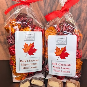 May include: Two clear cellophane bags tied with red ribbon, filled with individually wrapped chocolate candies. Each bag has a label with a maple leaf graphic and text: "Dark Chocolate Maple Cream Filled Leaves" and "Milk Chocolate Maple Cream Filled Leaves".