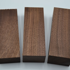 May include: Three rectangular pieces of walnut wood, each with a different grain pattern. The wood is a rich brown color.