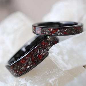 May include: Two black rings with a red and silver inlay design. The rings are stacked on top of each other.