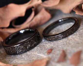 May include: Two black wedding bands with a textured, hammered finish. The bands are made of a durable metal and have a matte finish.