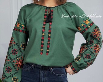 May include: A green long-sleeved shirt with embroidered floral patterns in red, orange, black, and yellow. The shirt has a round neckline and a tassel tie at the front. The text "Embroidery Style House" is visible in the top right corner of the image.